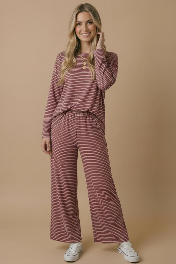 woman wearing a maroon and cream striped long sleeve top and matching wide-leg pants, posing casually