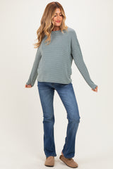 woman wearing a teal and white striped maternity top and blue flared jeans, smiling with a relaxed pose