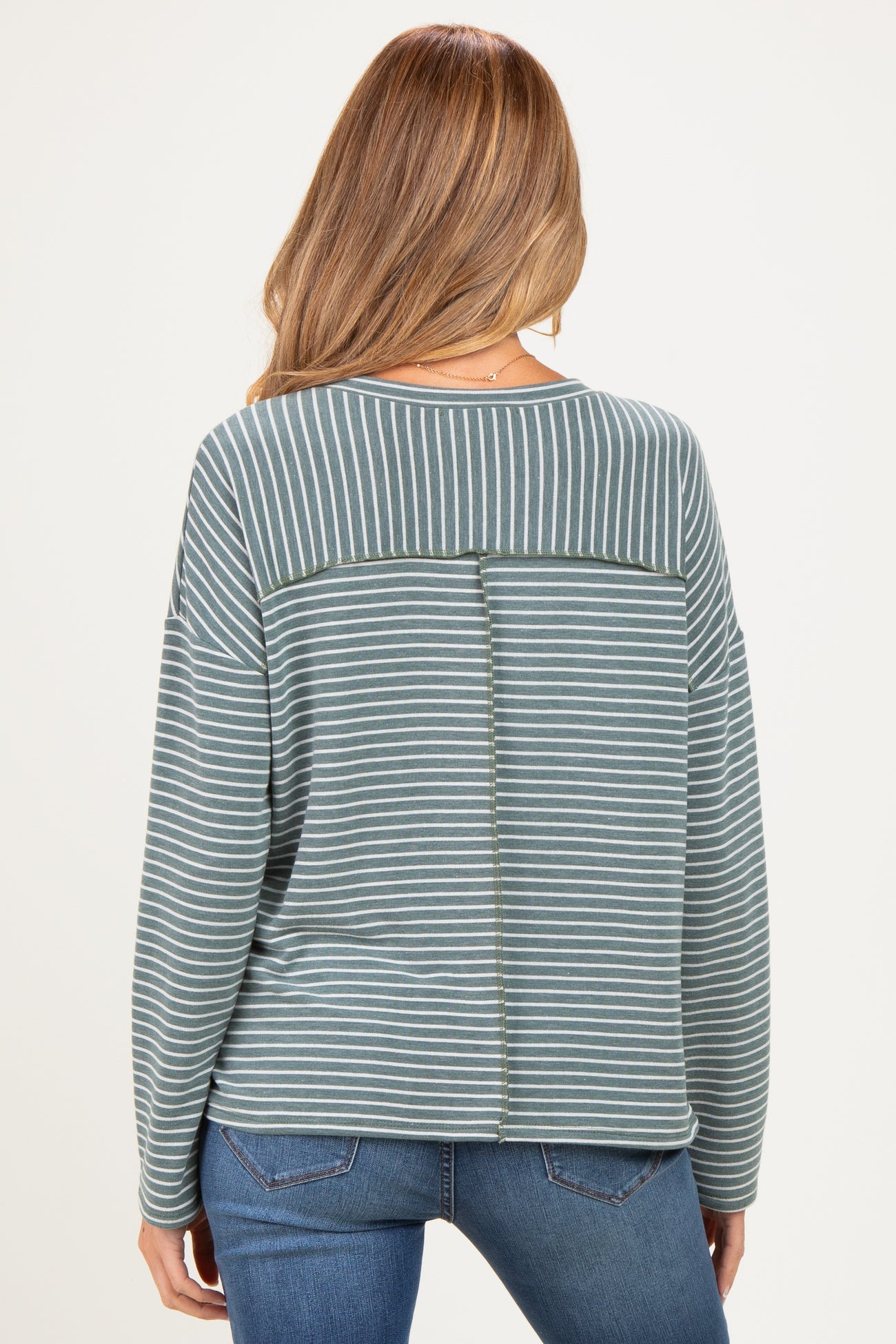woman wearing a striped green maternity sweatshirt with an open back detail, styled with blue jeans