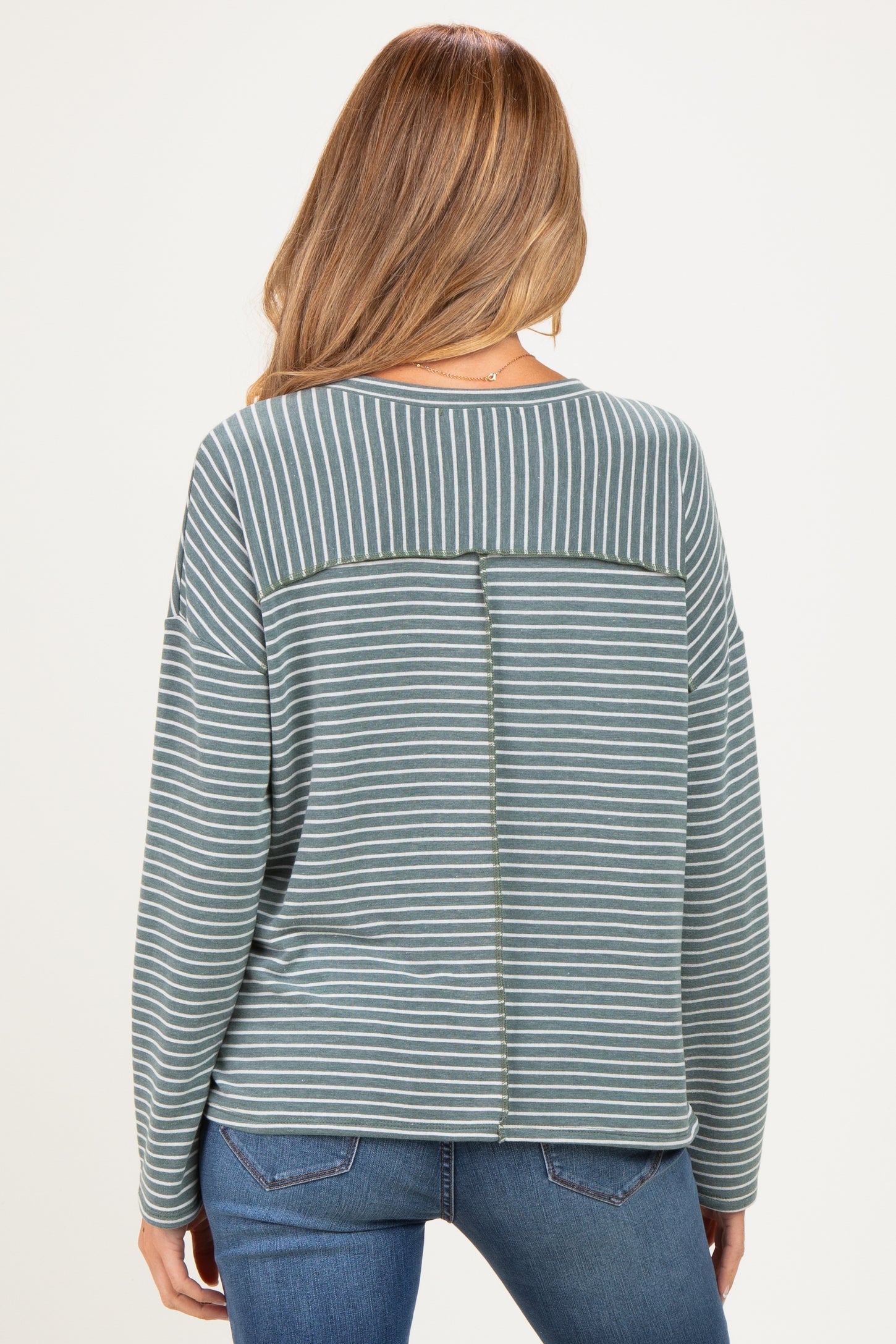 woman wearing a striped green maternity sweatshirt with an open back detail, styled with blue jeans