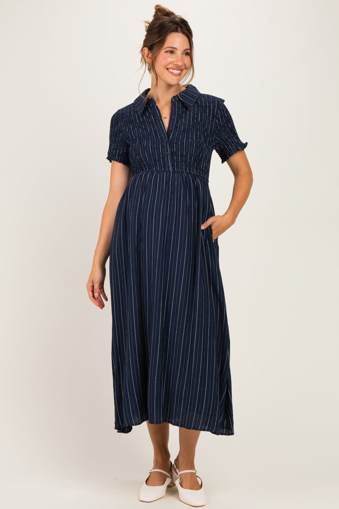 woman wearing a navy striped maternity dress with short sleeves and a collared neckline, holding her baby bump