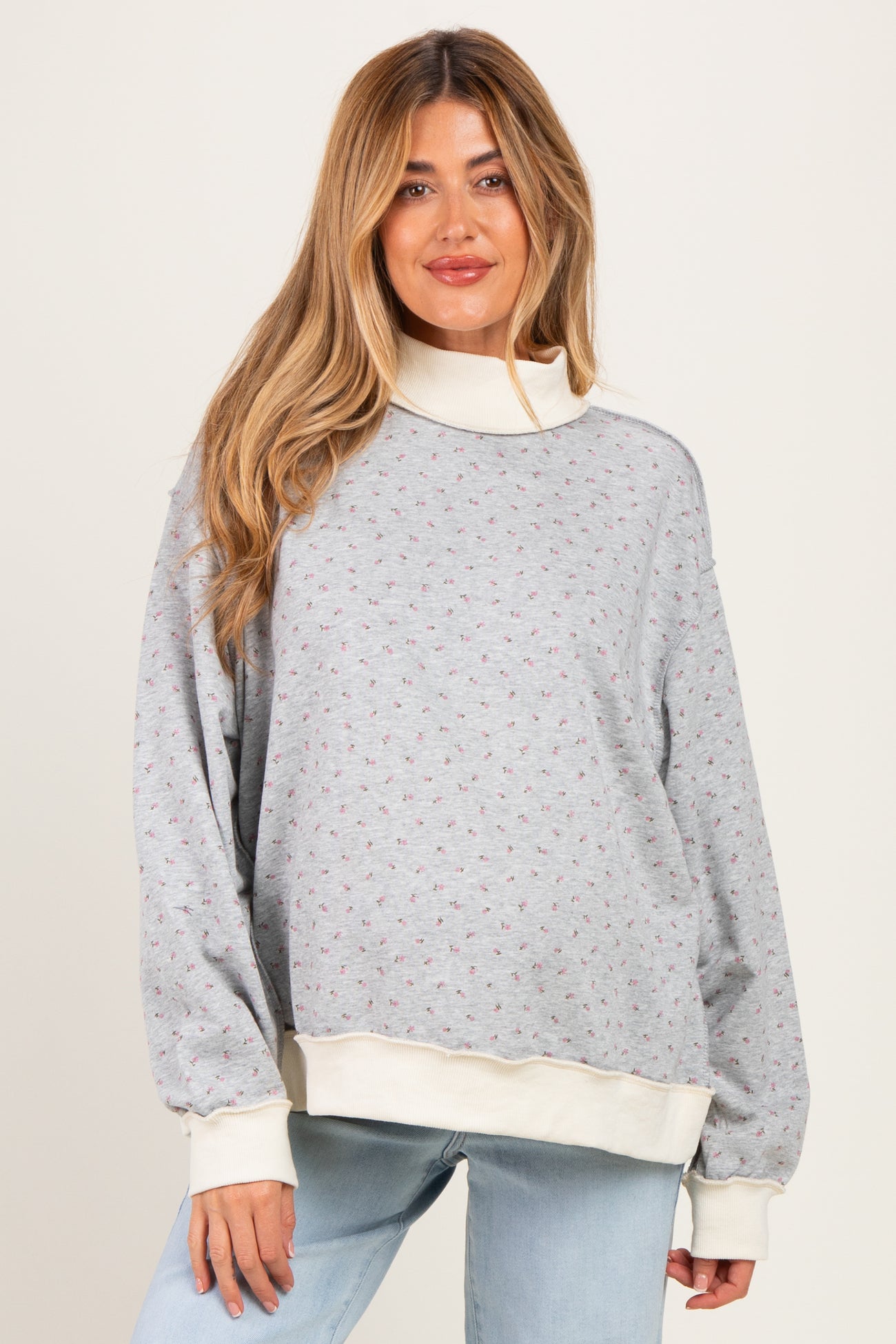 woman wearing a gray maternity sweatshirt with a floral pattern and cream-colored cuffs, styled casually