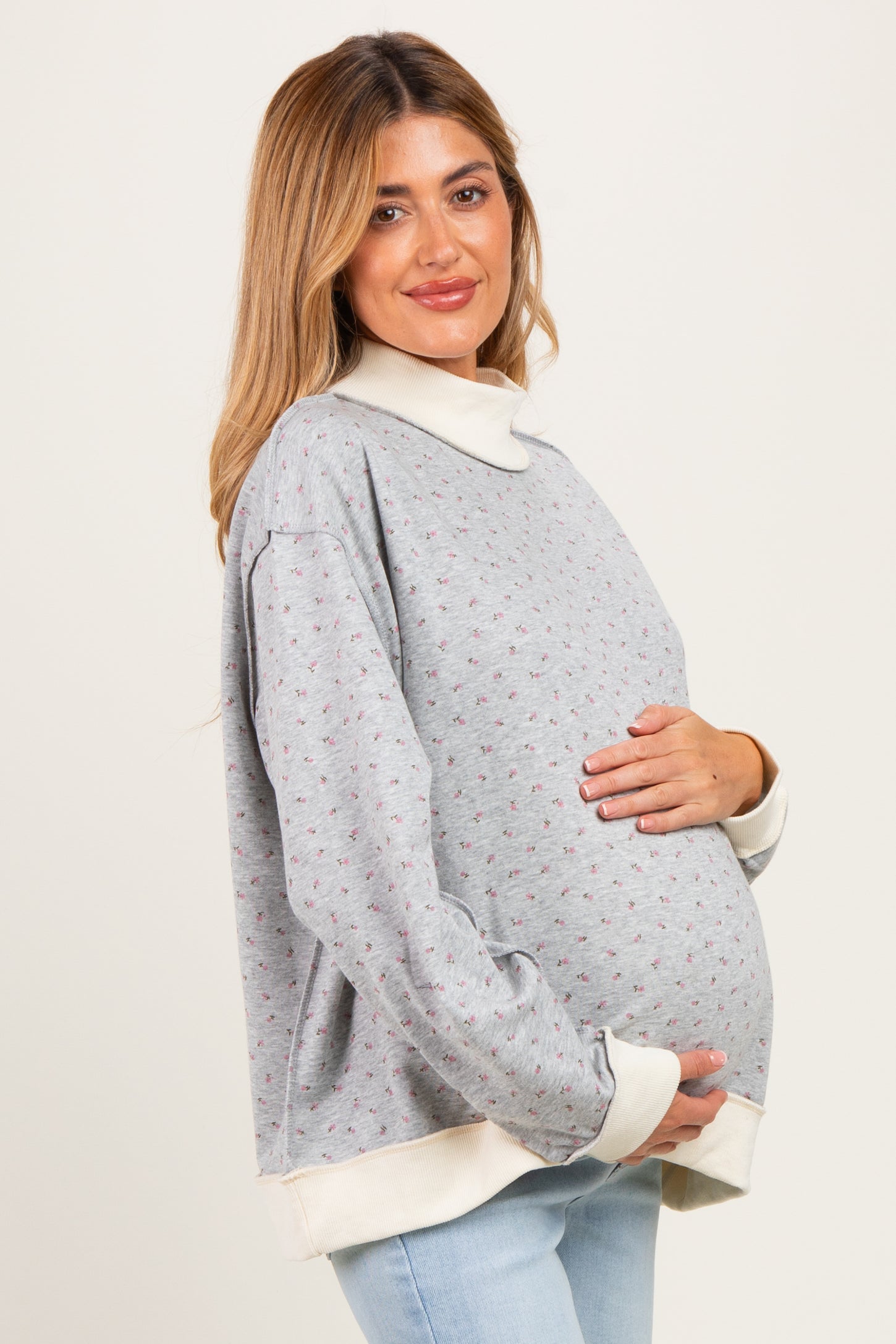 woman wearing a grey floral maternity sweatshirt with a white collar, holding her baby bump