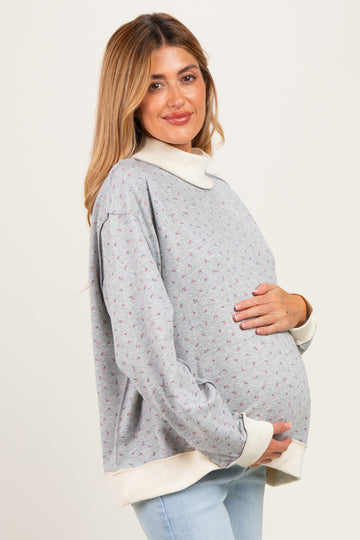 woman wearing a grey floral maternity sweatshirt with a white collar, holding her baby bump