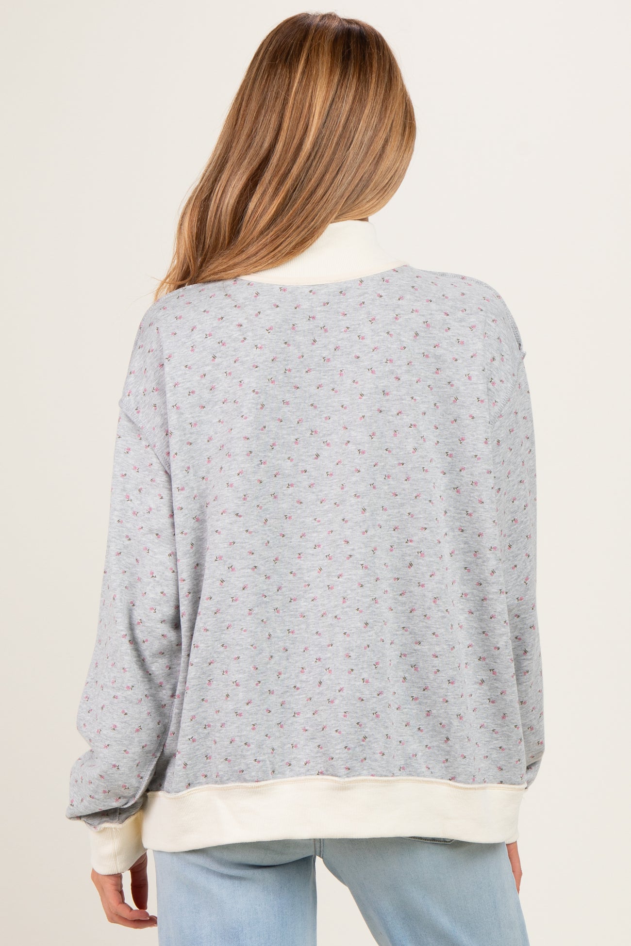 woman wearing a light gray maternity sweatshirt with a floral pattern and cream-colored trim, viewed from the back