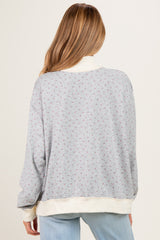 woman wearing a light gray maternity sweatshirt with a floral pattern and cream-colored trim, viewed from the back