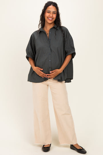 woman wearing a dark green plaid maternity shirt and beige wide-leg pants, cradling her baby bump