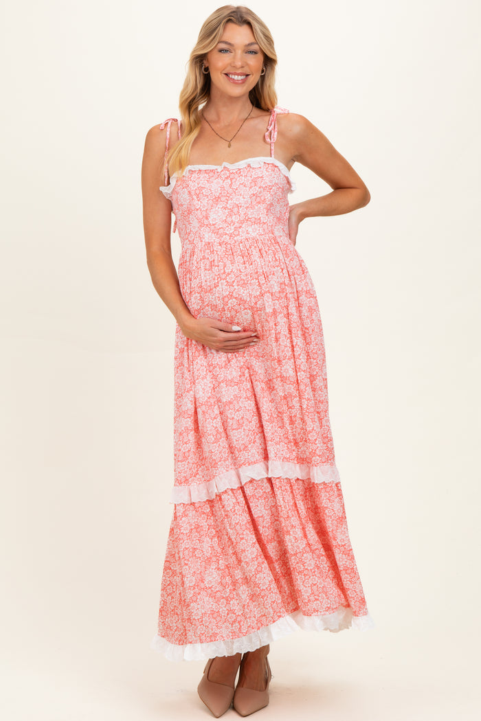 woman wearing a pink floral maternity maxi dress with ruffled straps and holding her baby bump
