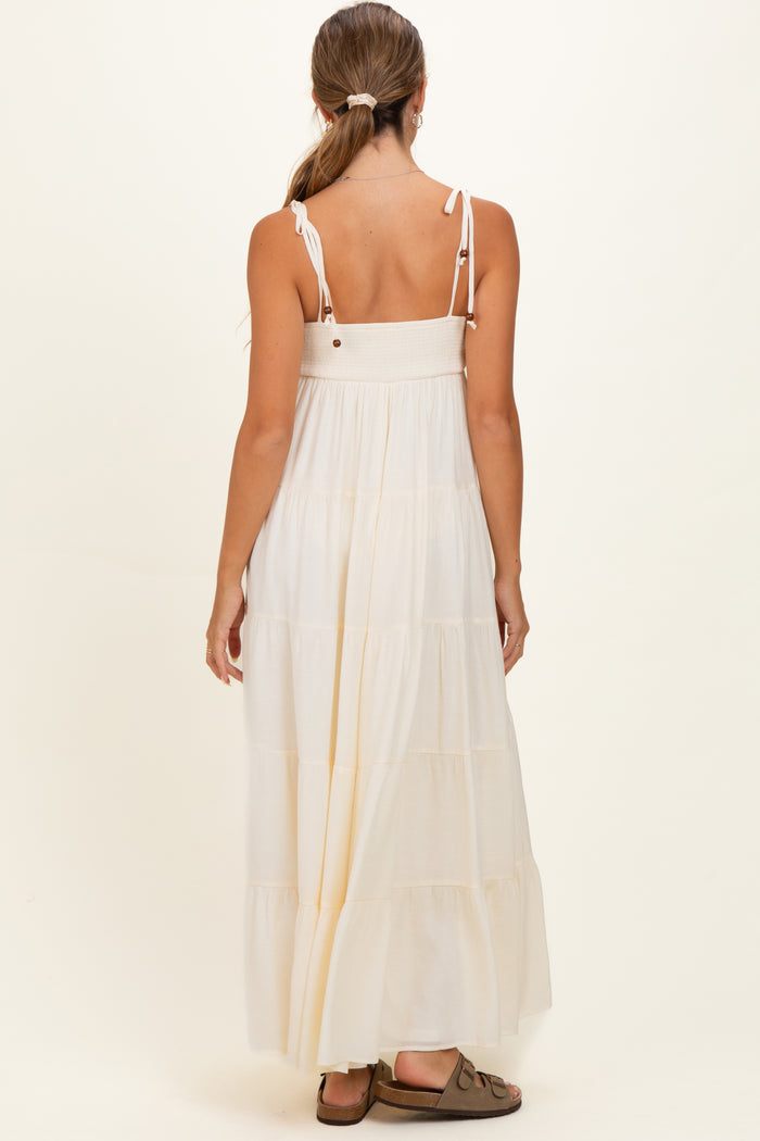 woman wearing a white tiered maxi maternity dress with adjustable straps and a smocked bodice, showing her back