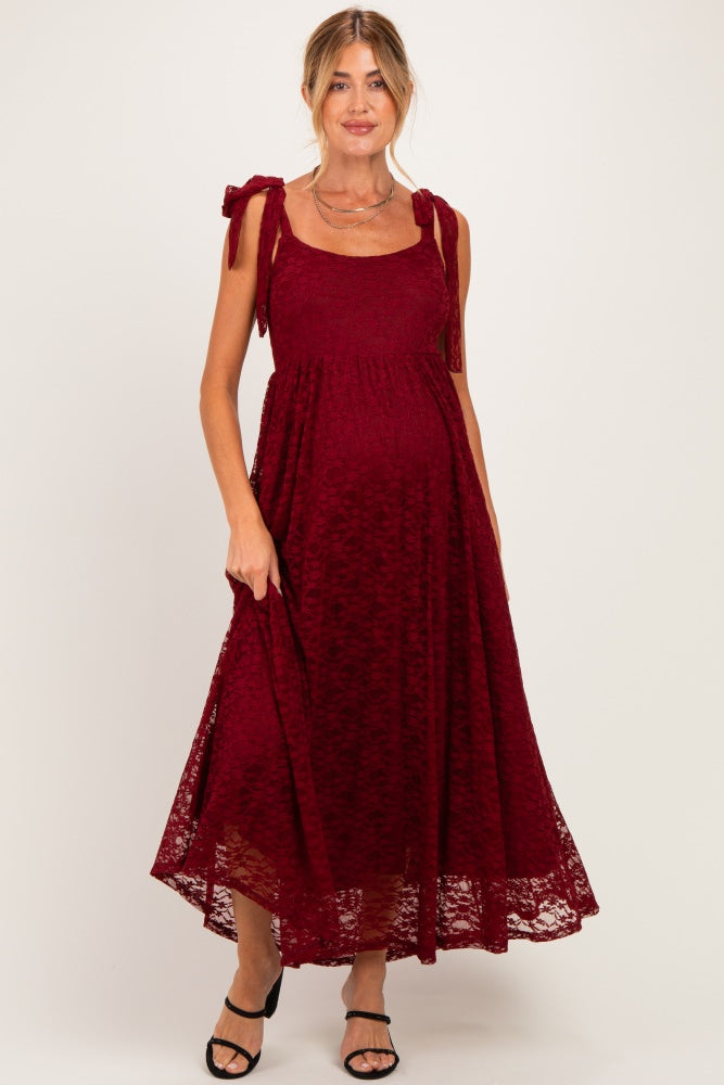 woman wearing a burgundy lace maternity dress with tied shoulder straps and a flowing skirt, showcasing her baby bump
