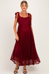 woman wearing a burgundy lace maternity dress with tied shoulder straps and a flowing skirt, showcasing her baby bump