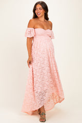 woman wearing a pink off-the-shoulder lace maternity dress with a fitted bodice and flowy skirt, showcasing her baby bump