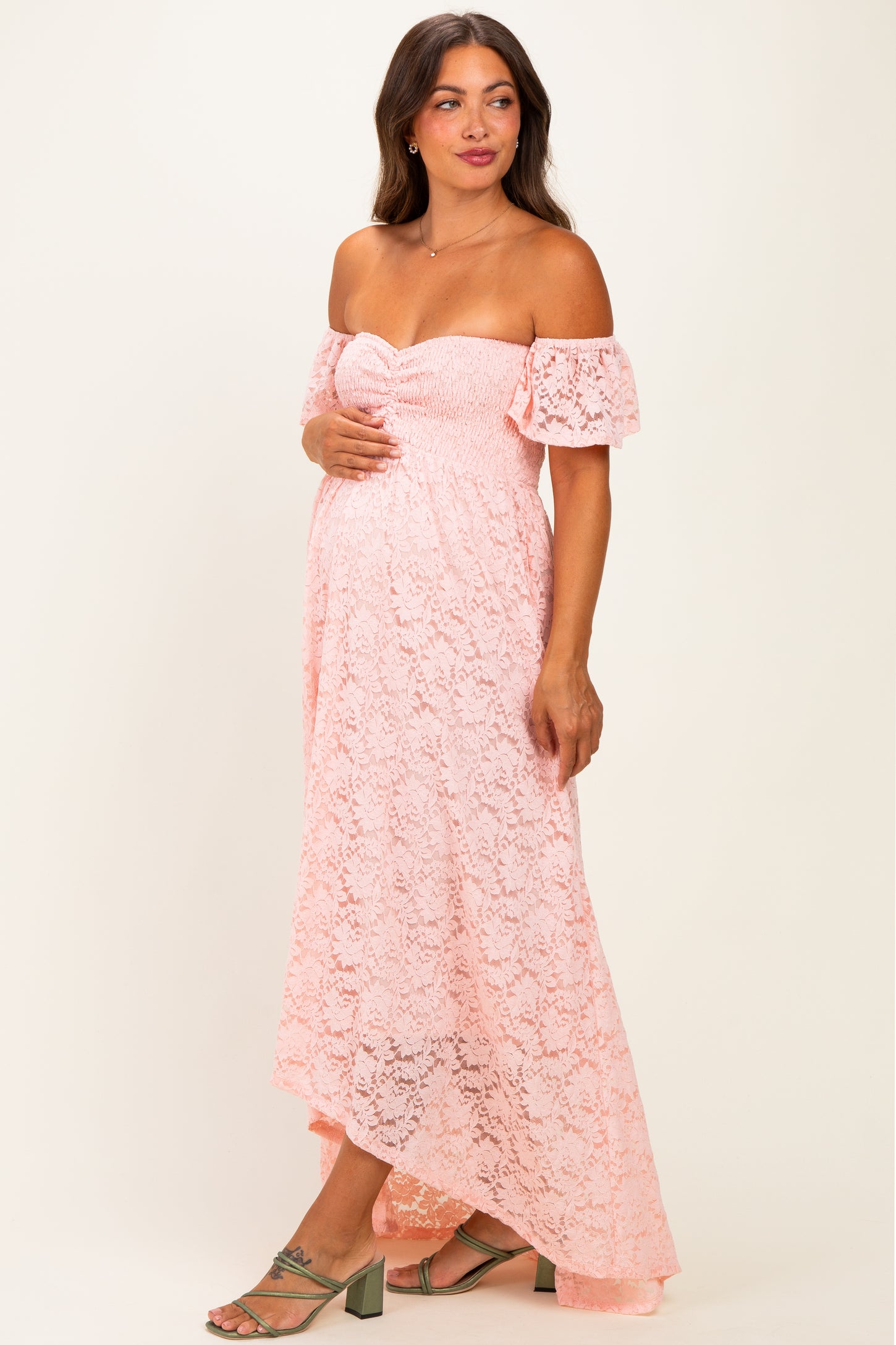 woman wearing a pink lace off-the-shoulder maternity dress with a fitted bodice and flowy hemline, showing her baby bump