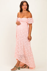 woman wearing a pink lace off-the-shoulder maternity dress with a fitted bodice and flowy hemline, showing her baby bump