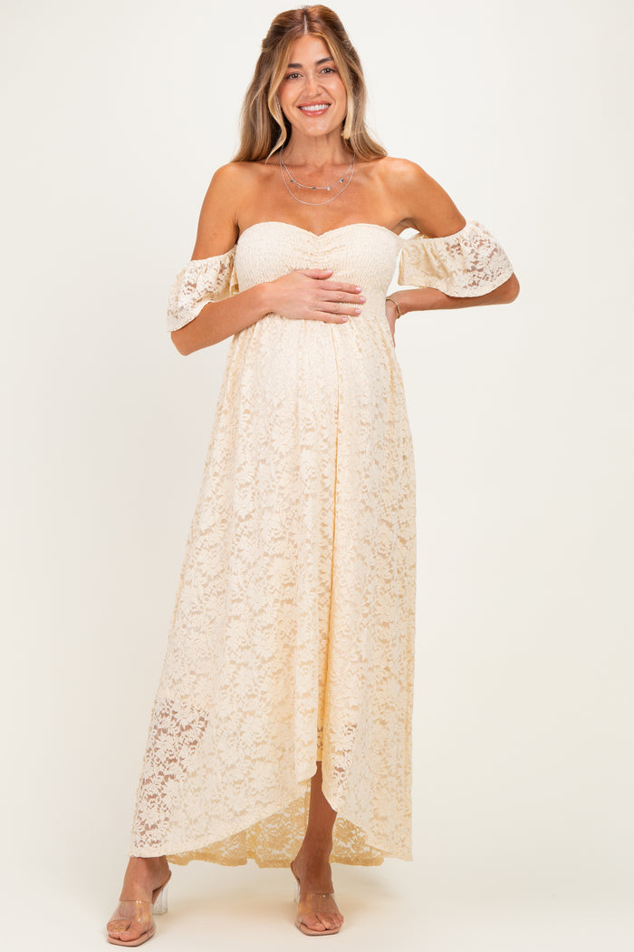 woman wearing a cream lace off-shoulder maternity dress and holding her baby bump