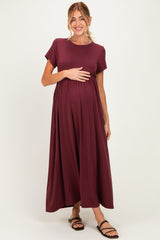 woman wearing a burgundy short sleeve maternity dress with a flowy skirt and holding her baby bump