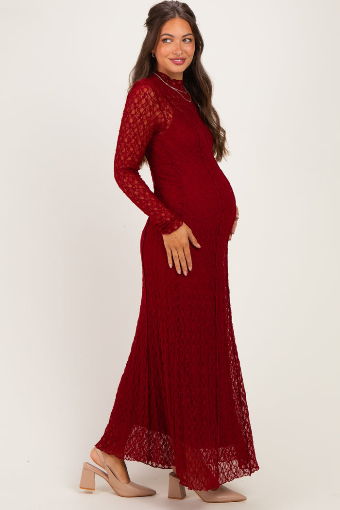 woman wearing a burgundy lace maternity dress with long sleeves and a flowing skirt, showing her baby bump