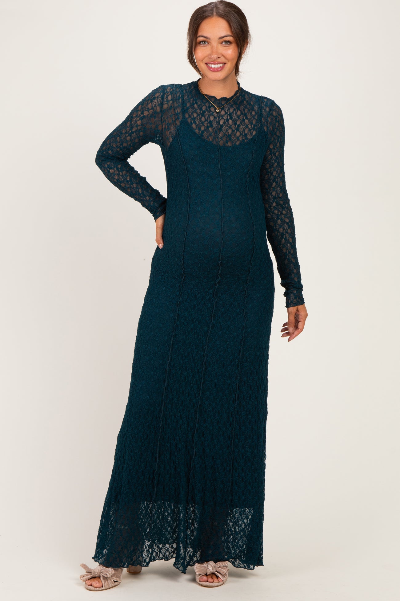 woman wearing a dark teal lace maternity dress with long sleeves and a fitted silhouette, showing her baby bump