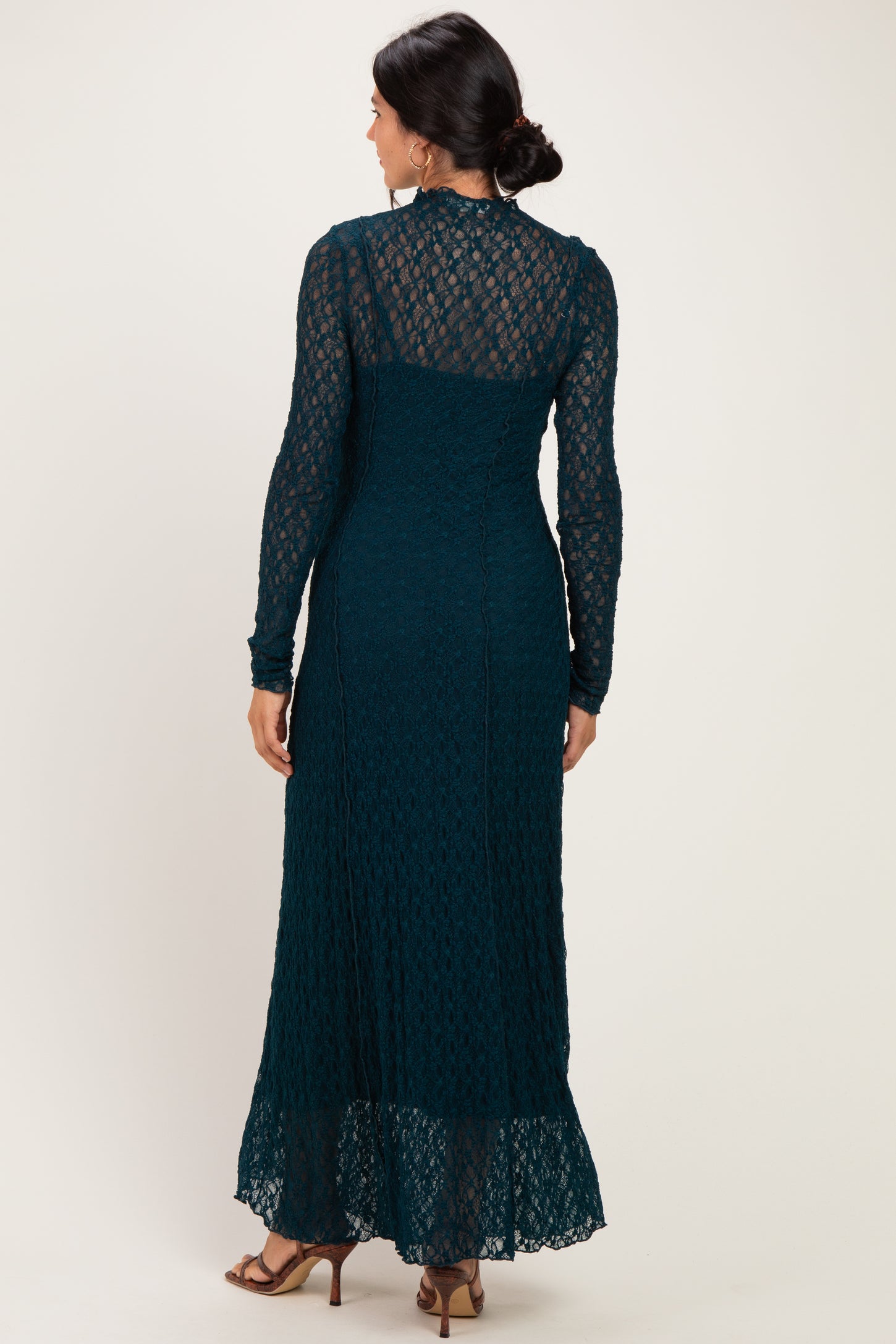 woman wearing a teal long sleeve maxi dress with a lace design and a flared hem, featured from the back