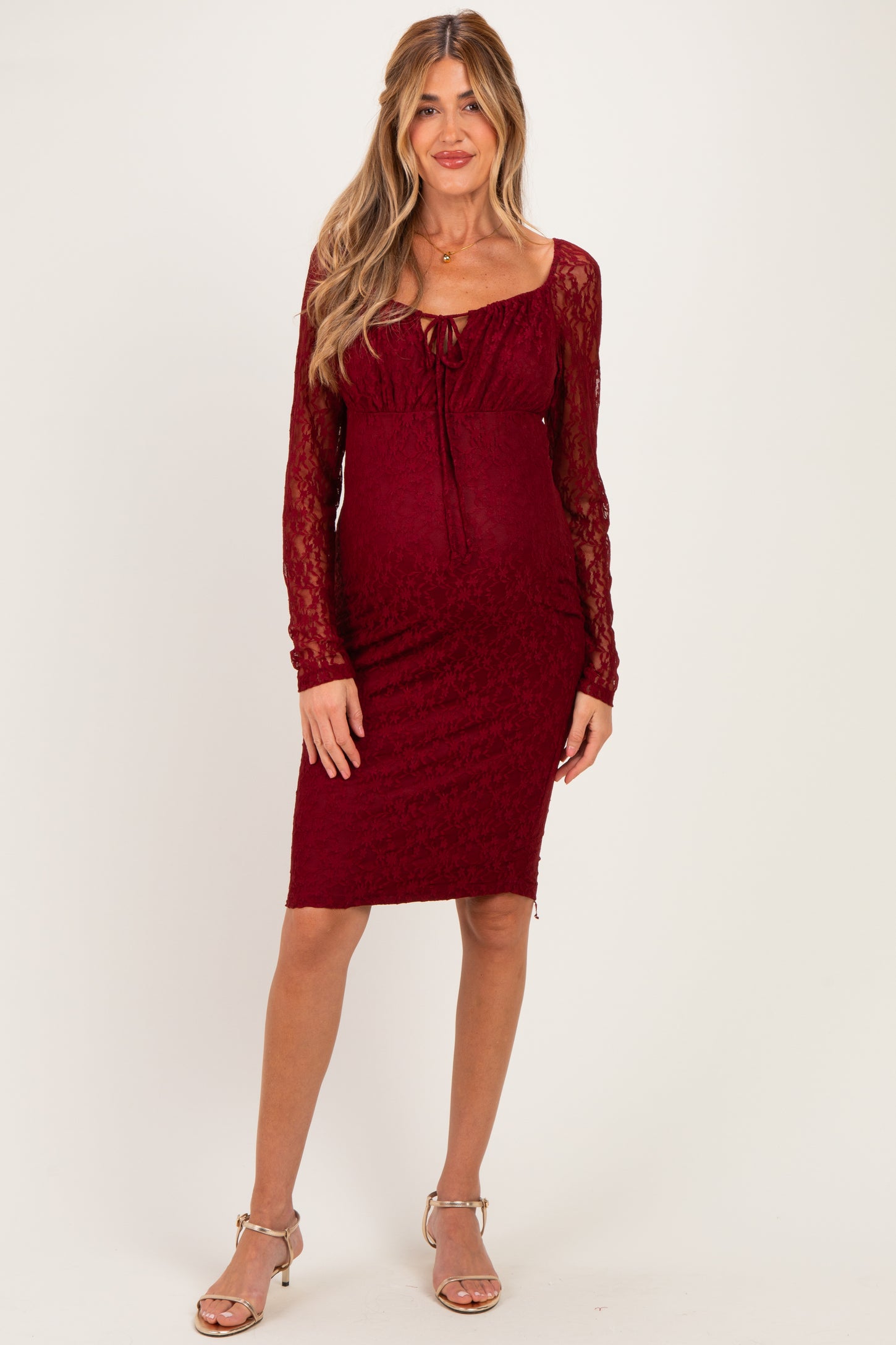 woman wearing a burgundy lace long sleeve maternity dress with a fitted silhouette and a sweetheart neckline, showcasing her baby bump