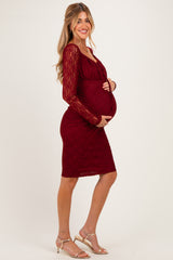 woman wearing a burgundy lace maternity dress, holding her baby bump, with long sleeves and a fitted silhouette