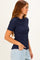 woman wearing a navy ribbed short sleeve top and light blue jeans, standing sideways with one hand in her pocket