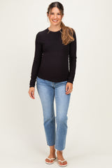 woman wearing a black long sleeve maternity top and blue jeans, displaying a baby bump