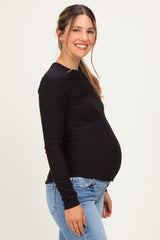 woman wearing a black long sleeve maternity top and showing her baby bump while smiling