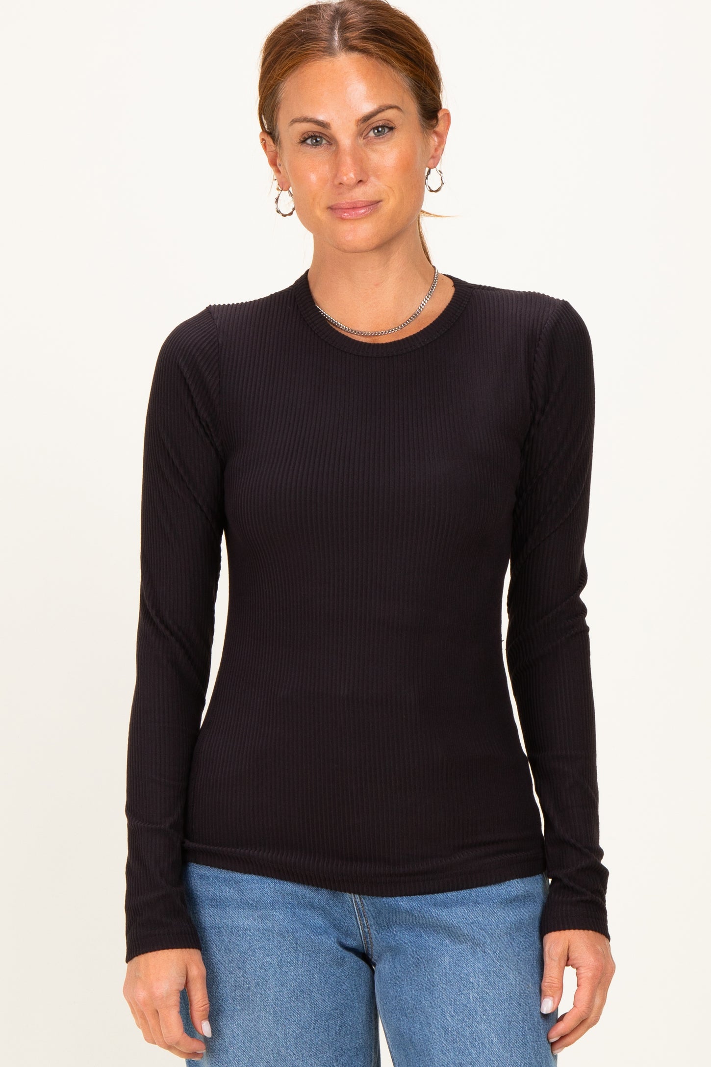 woman wearing a black ribbed long sleeve top with a fitted style and round neckline, paired with blue jeans