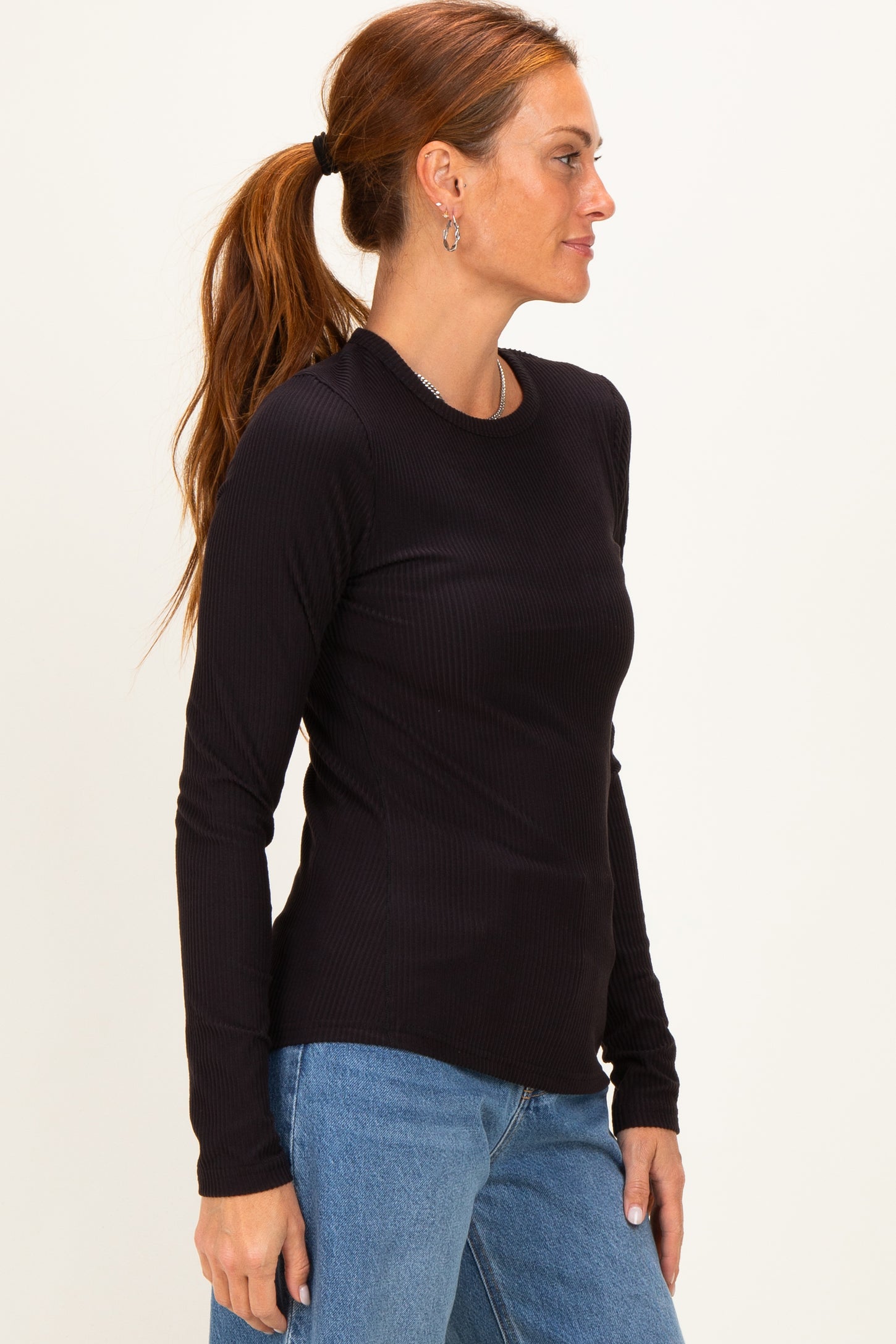 woman wearing a black long sleeve ribbed top with round neckline and side profile view