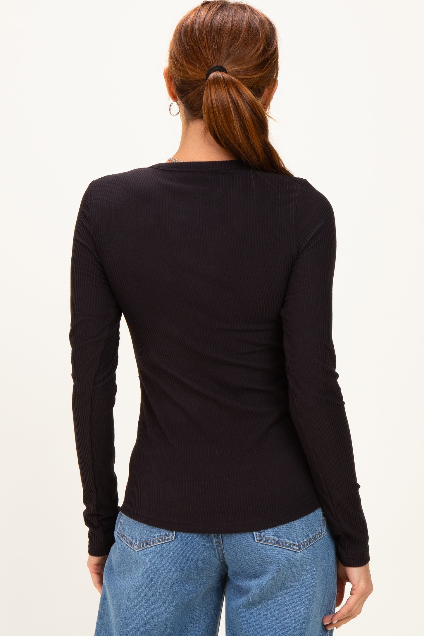 woman wearing a black fitted long sleeve ribbed top, viewed from the back with loose blue jeans