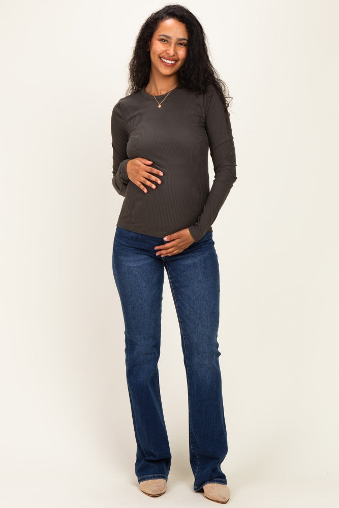 woman wearing a dark green ribbed long sleeve maternity top and holding her baby bump, paired with blue jeans