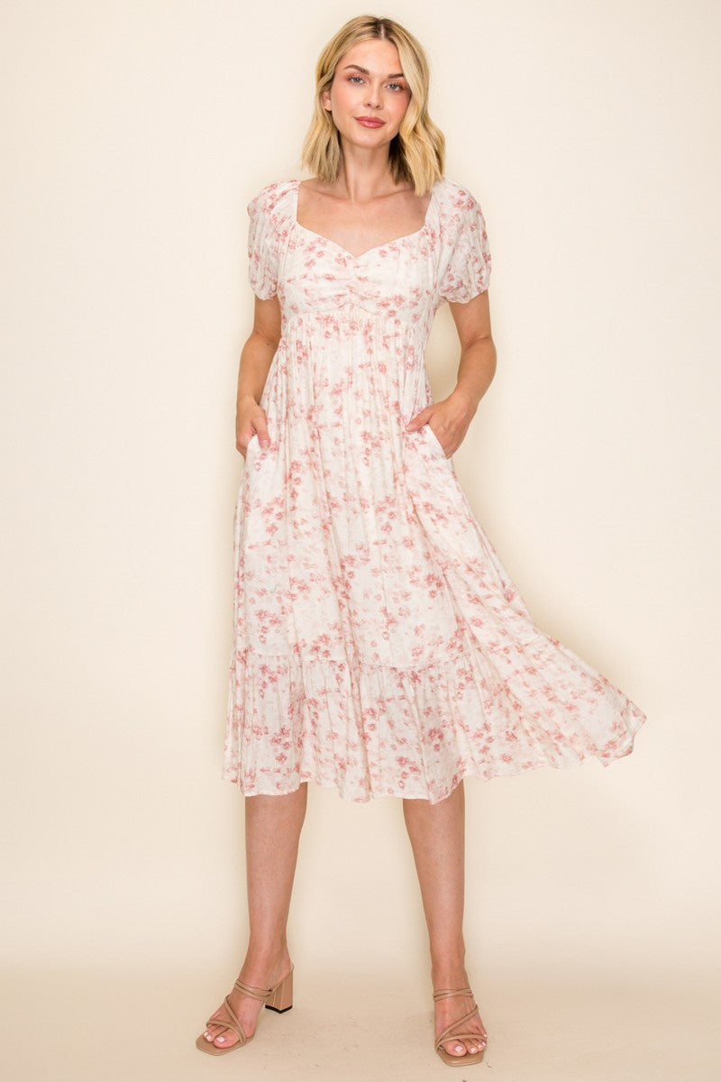 woman wearing a light pink floral midi dress with puff sleeves and pockets