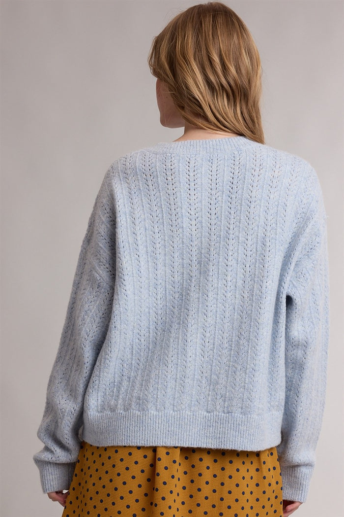 woman wearing a light blue knitted sweater with a relaxed fit, seen from the back, paired with a mustard polka dot skirt