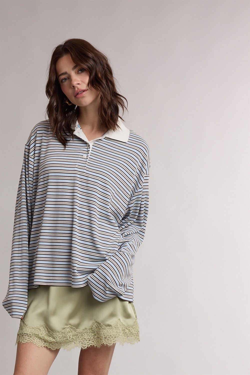 woman wearing a striped oversized long sleeve polo shirt with a white collar and a satin green mini skirt with lace trim