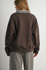 woman wearing a brown oversized sweatshirt with a checked collar, styled with checked pants