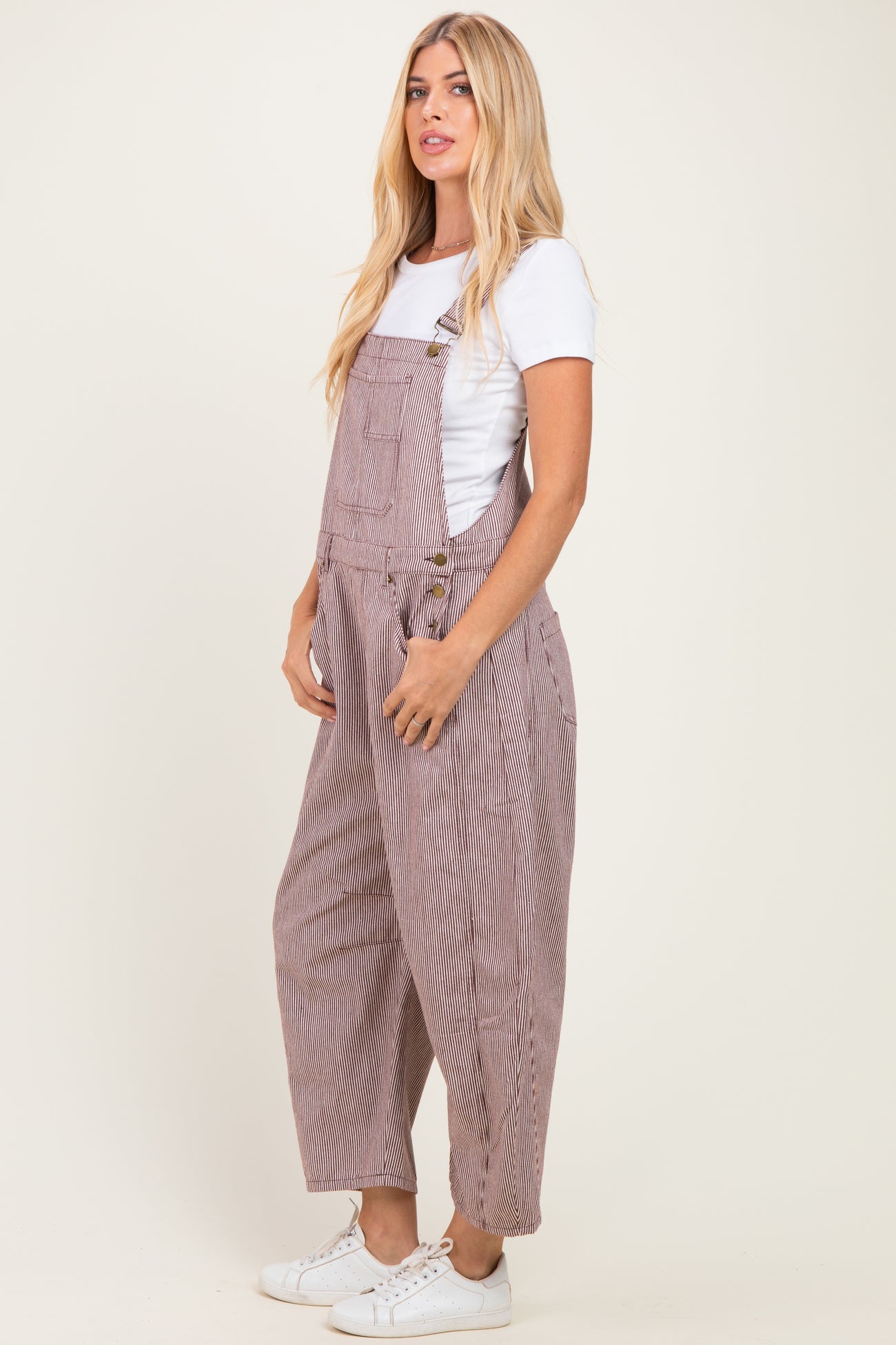 woman wearing beige and white striped overalls over a white t-shirt with pockets and rolled up cuffs, styled casually