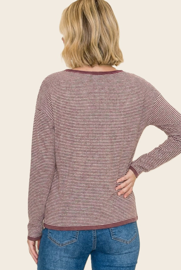 woman wearing a maroon and white striped long sleeve top, viewed from the back, paired with blue jeans