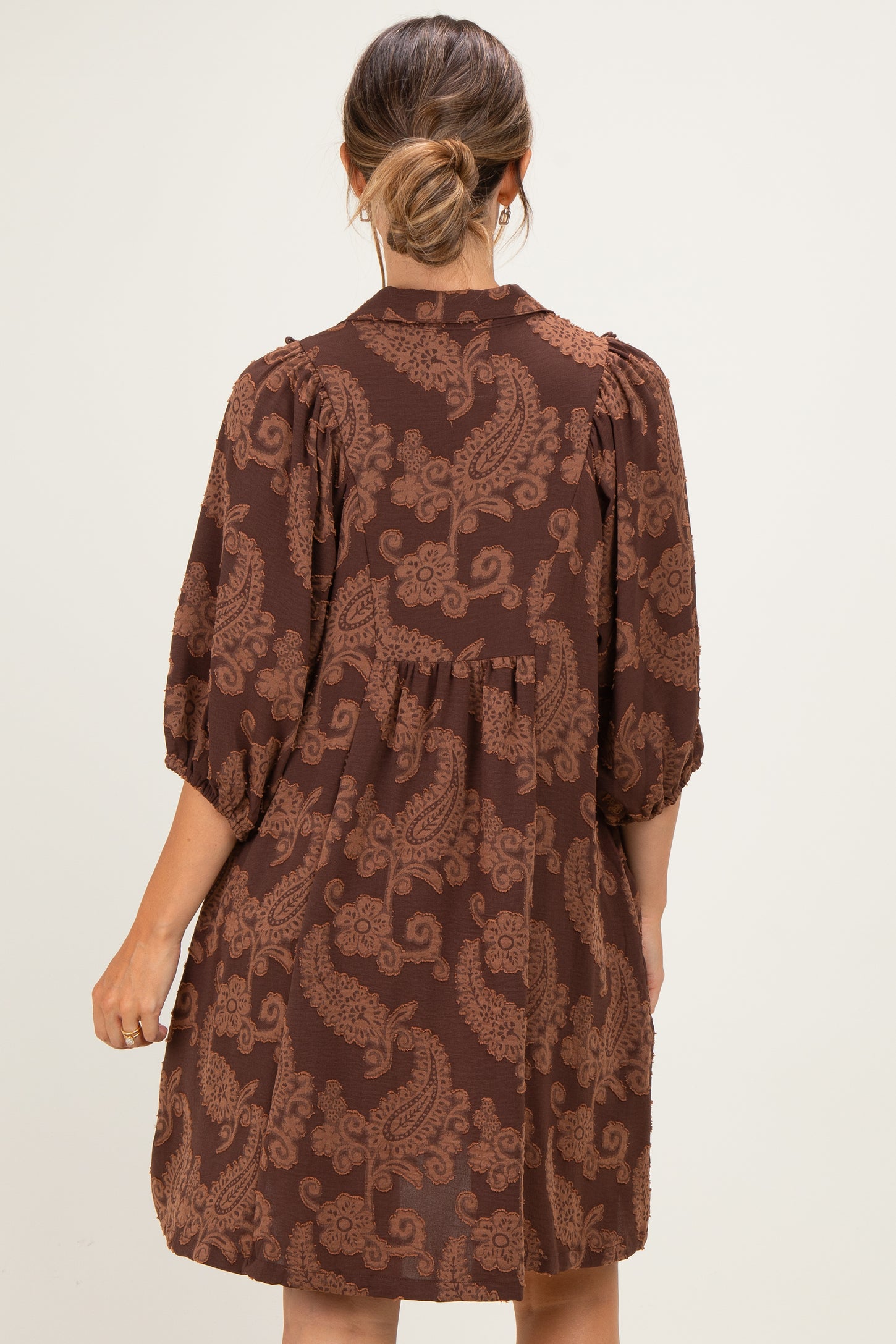 woman wearing a brown paisley print maternity dress with a loose fit and puff sleeves from the back