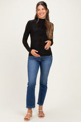 woman wearing a black long sleeve maternity top with floral pattern and blue flared jeans, holding her baby bump