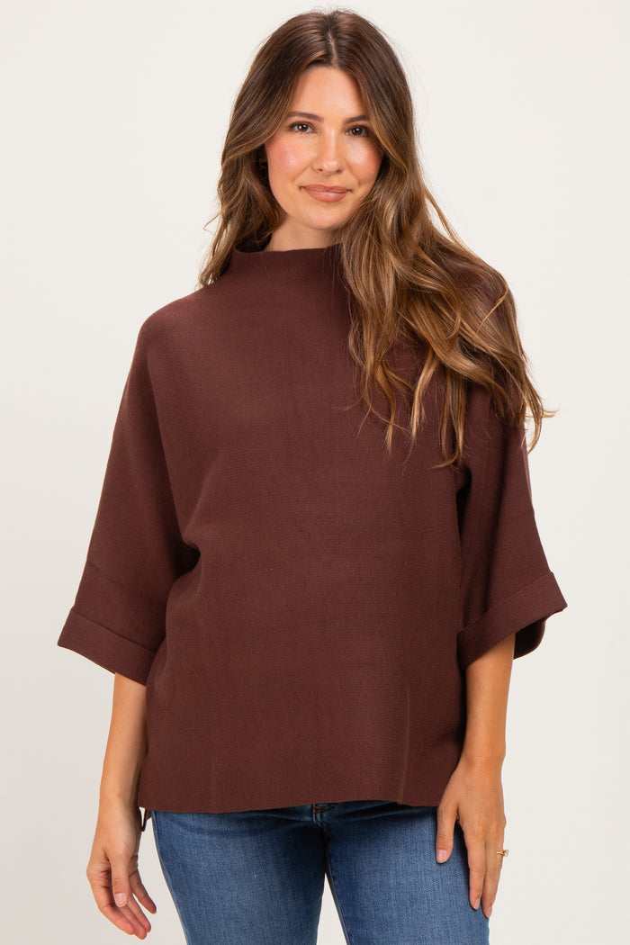 woman wearing a brown maternity top with a high neckline and short sleeves, paired with blue jeans
