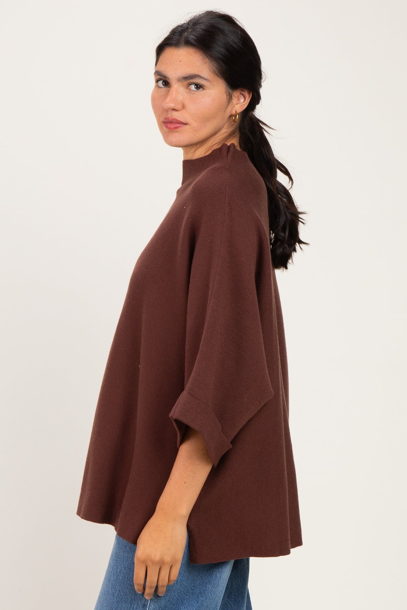 woman wearing a brown oversized sweater with a high neckline and wide sleeves, styled with blue jeans
