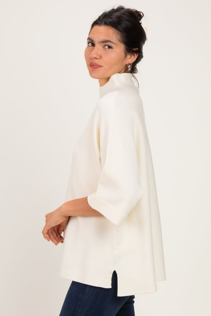 woman wearing a cream oversized top with three-quarter sleeves and side slits, paired with dark jeans