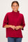 woman wearing a crimson oversized sweater with a high neck and relaxed fit, styled with blue jeans