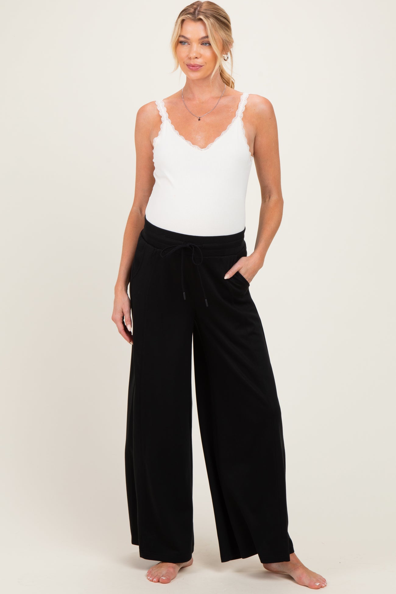 woman wearing a white lace trim maternity tank top and black wide-leg maternity pants with pockets