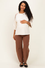 woman wearing a cream maternity top with three-quarter sleeves and brown maternity pants, holding her baby bump