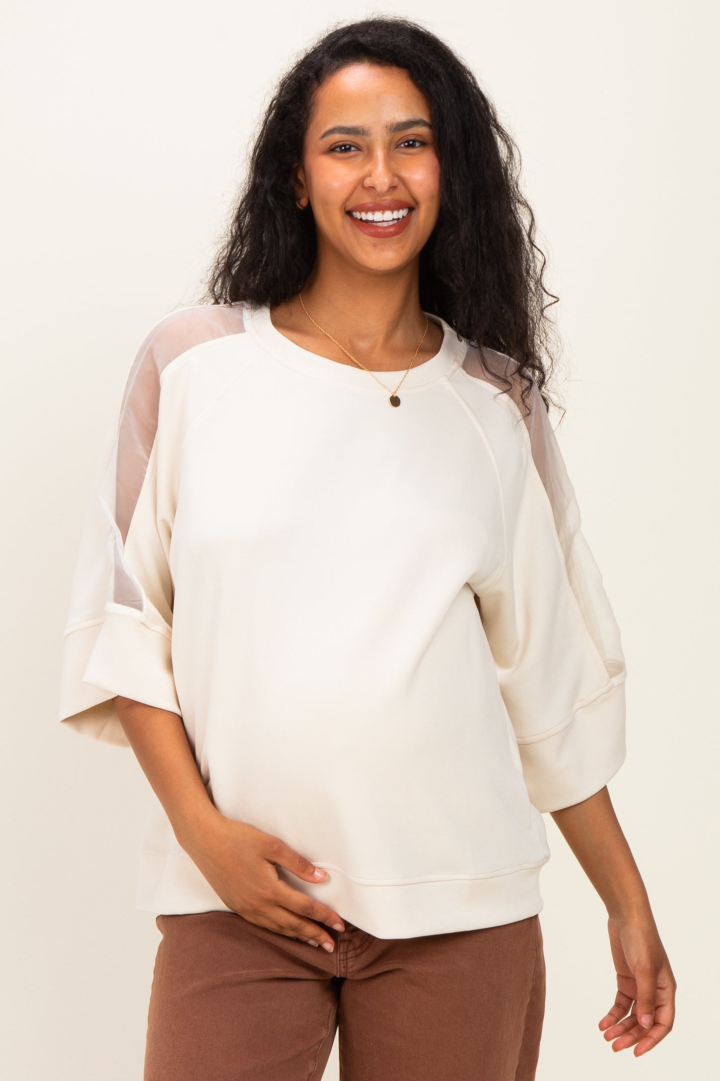 woman wearing a cream maternity sweatshirt with sheer details and holding her baby bump