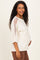 woman wearing a cream maternity top with sheer sleeves and a visible baby bump, smiling and standing sideways