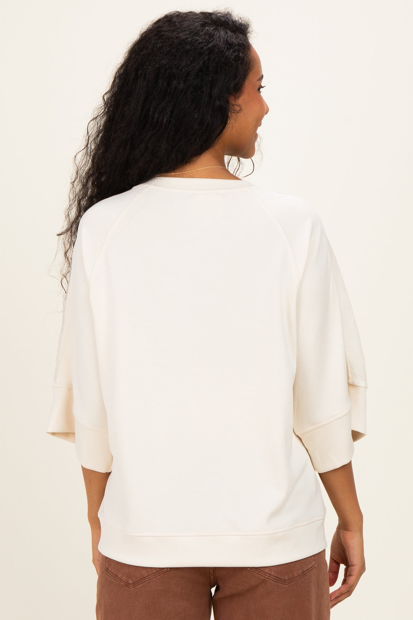woman wearing a light cream oversized maternity sweatshirt, showing the back view with relaxed sleeves