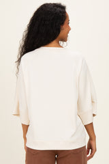 woman wearing a light cream oversized maternity sweatshirt, showing the back view with relaxed sleeves